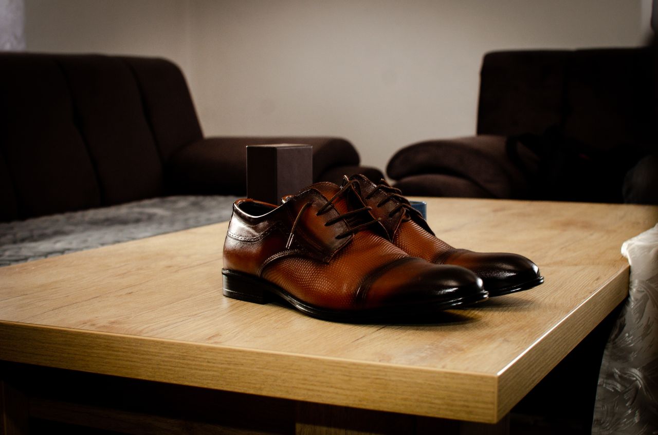 about-us Stylish brown leather shoes placed on a wooden table in a cozy indoor setting.