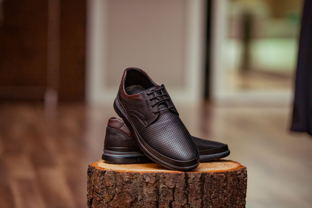 heros-img Stylish perforated leather shoes displayed elegantly on a rustic wooden stump indoors.